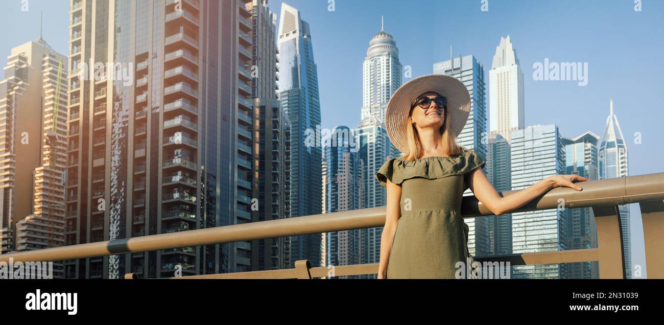 Donna alla moda con vestito verde e cappello che gode dell'architettura della città di Dubai. Viaggio negli Emirati Arabi Uniti. banner con spazio di copia Foto Stock