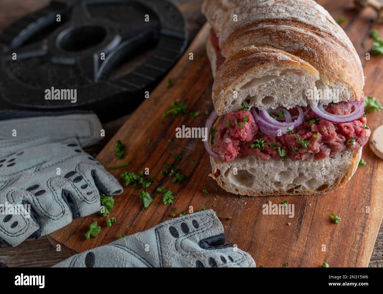 Sandwich proteico con tataro di manzo su un rustico pane baguette con cipolle rosse e prezzemolo su tavola di legno Foto Stock