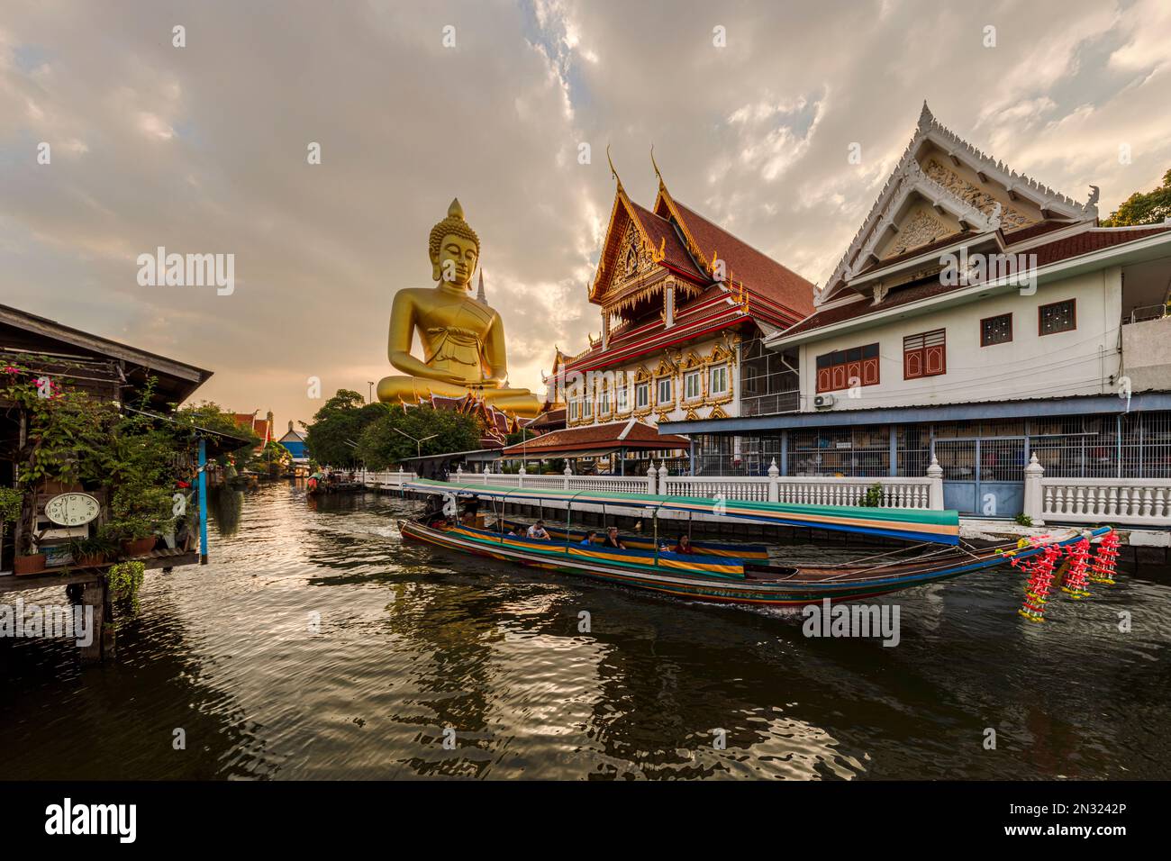 Una barca passava la statua del Grande Buddha (Phra Buddha Dhammakaya Thepmongkhon) nel tempio Wat Pak Nam Phasi Charoen situato vicino al fiume durante il tramonto. Foto Stock