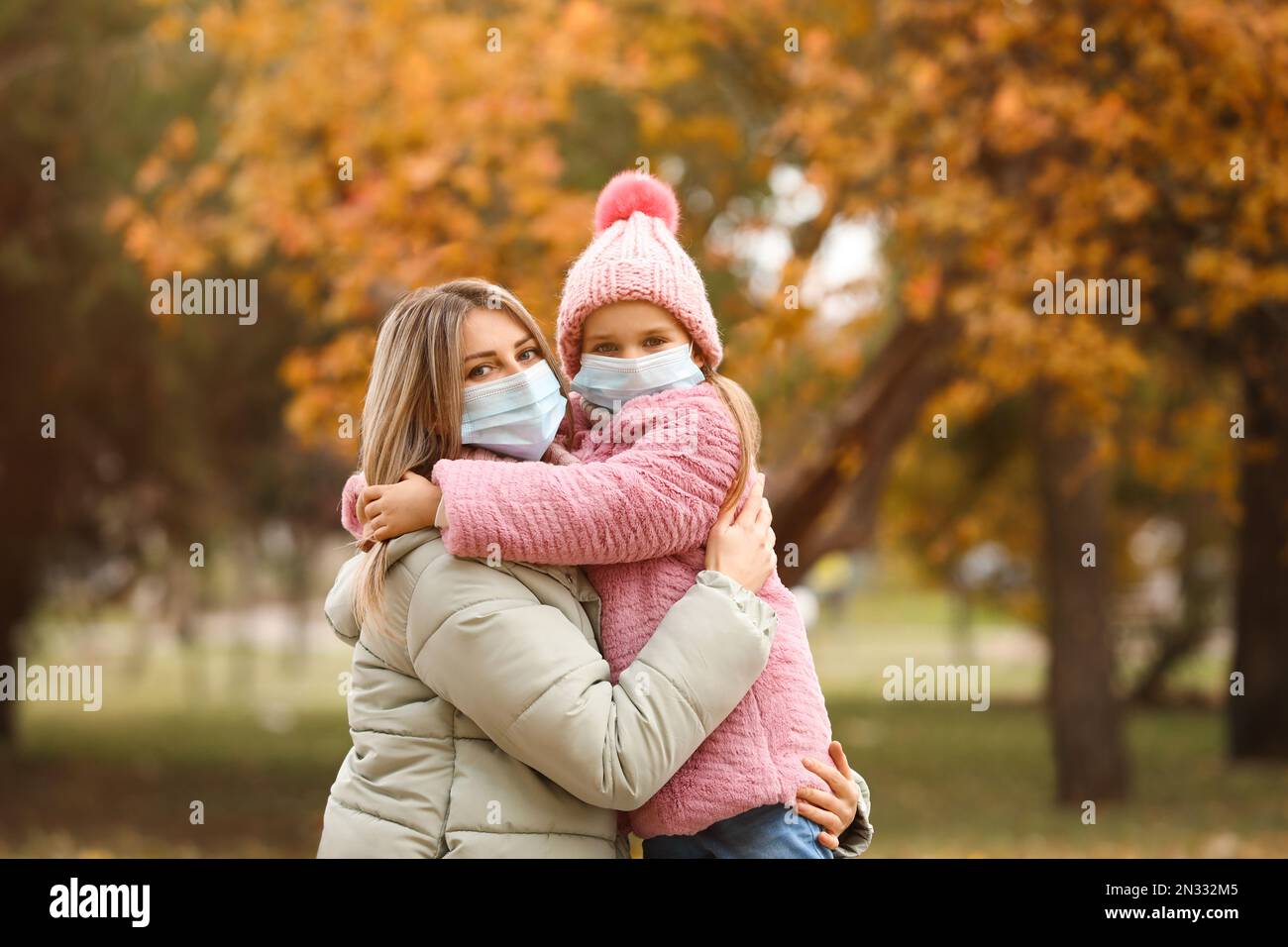 Madre e figlia in maschere mediche all'aperto il giorno d'autunno. Misure protettive durante la quarantena del coronavirus Foto Stock