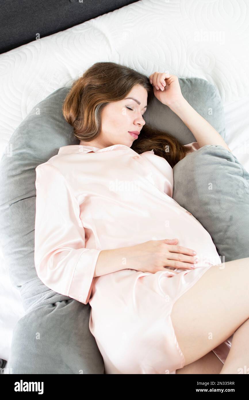 Dormire in un cuscino di gravidanza donna incinta caucasica. Comfort nel dormire in gravidanza. Cuscino per il corpo maternità Foto Stock