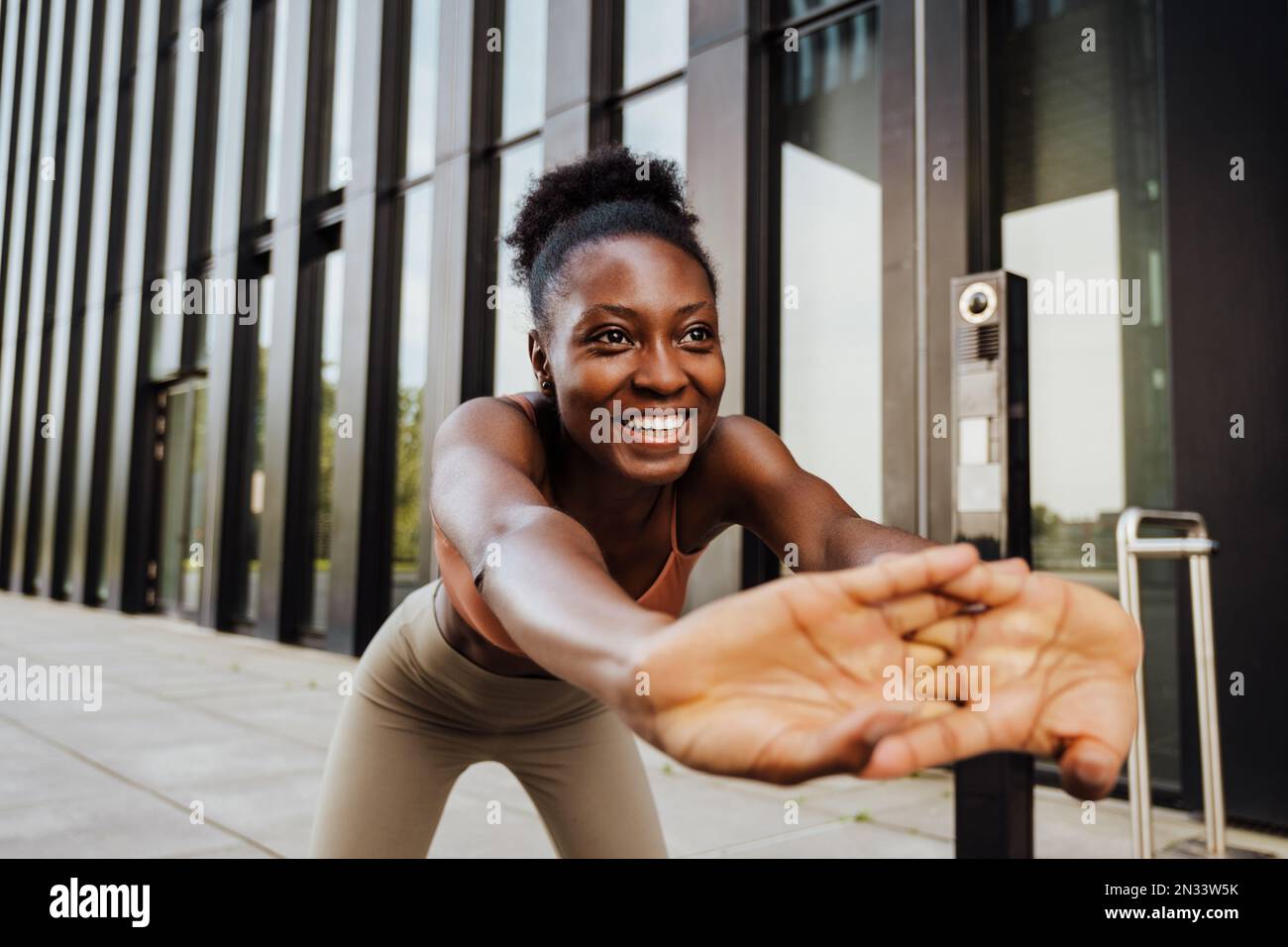 Giovane bella sportiva sorridente felice donna africana che allunga la schiena piegandosi con le mani intrecciate e guardando da parte , mentre si trova all'aperto Foto Stock