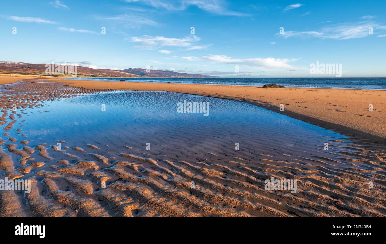 La spiaggia di Brora nelle Highlands con la marea che guarda a nord sulle ondulazioni di sabbia verso le colline di Sutherland Foto Stock