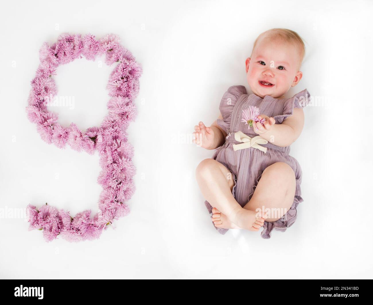 Piccola bambina neonato in un rompero viola. bambino di 9 mesi. Traguardo  di nove mesi per il bambino Foto stock - Alamy