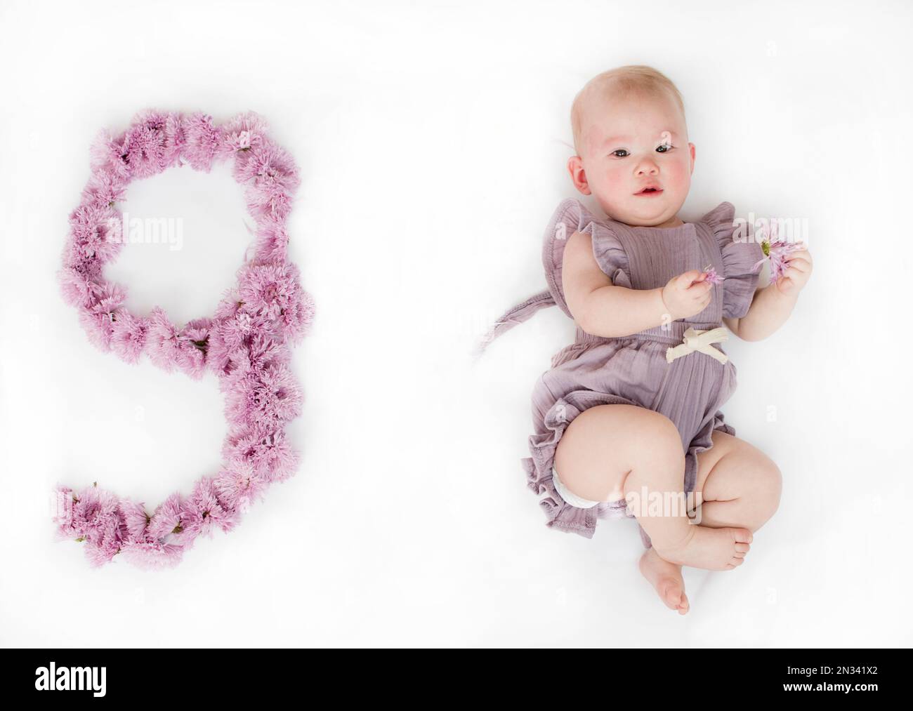 Piccola bambina neonato in un rompero viola. bambino di 9 mesi. Traguardo  di nove mesi per il bambino Foto stock - Alamy