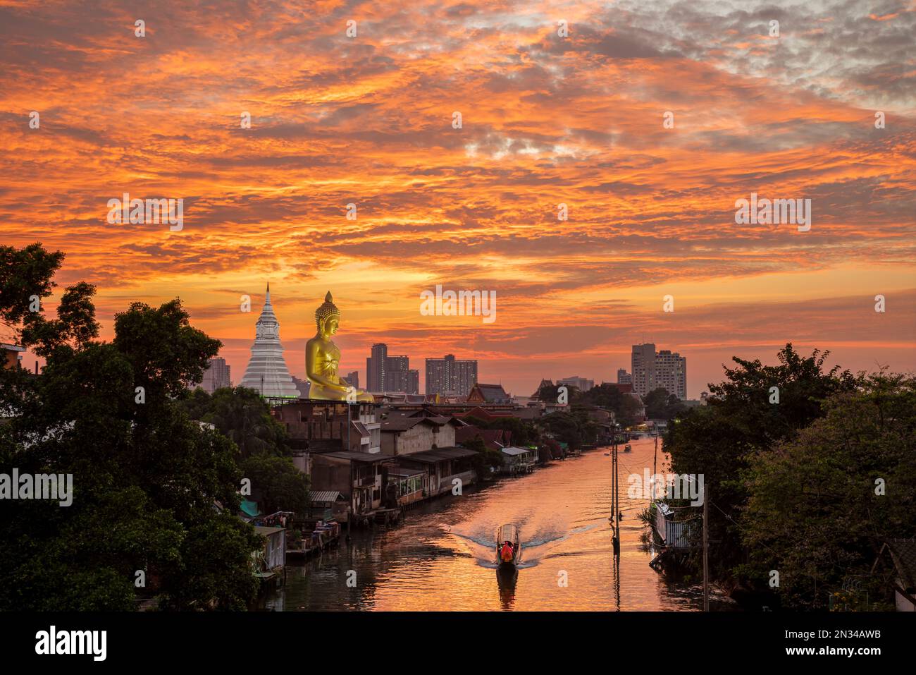Una barca passava la statua del Grande Buddha (Phra Buddha Dhammakaya Thepmongkhon) nel tempio Wat Pak Nam Phasi Charoen situato vicino al fiume durante il tramonto. Foto Stock