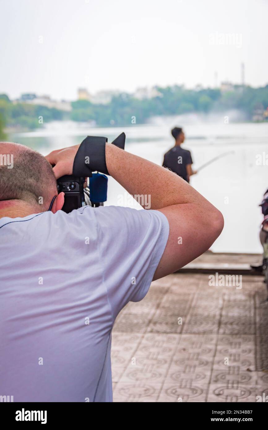 Fotografia di backstage, retro di un uomo fotografo scattare una foto di un uomo di pesca presso un lago. Foto Stock