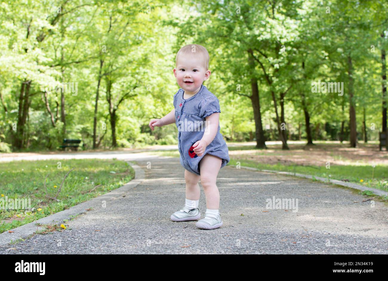 Un bambino sta facendo i suoi primi passi nel parco. Il bambino sta imparando come camminare. Sviluppo del bambino 1-year-old ragazza Foto Stock