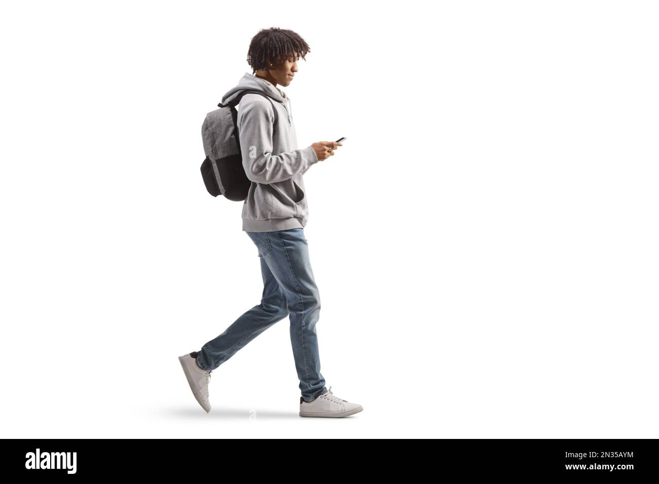 Profilo a tutta lunghezza di un maschio afro-americano con uno zaino a piedi e utilizzando un telefono cellulare isolato su sfondo bianco Foto Stock