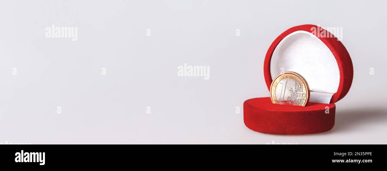 Scatola regalo rossa con una moneta in euro, valuta ufficiale della zona euro. Moneta dell'Unione europea presentata come gioielli su sfondo bianco con spazio copia. Foto Stock