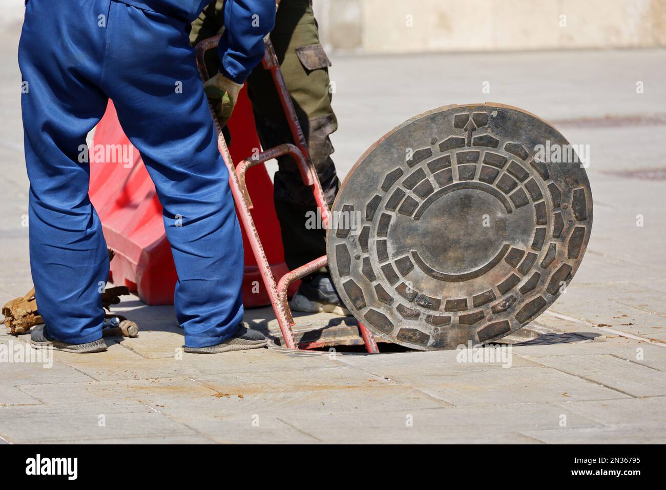 I lavoratori che si erlevano in piedi sul portello aperto della fogna su una strada. Riparazione di fognature, impianti sotterranei, impianti di alimentazione idrica, posa di cavi Foto Stock
