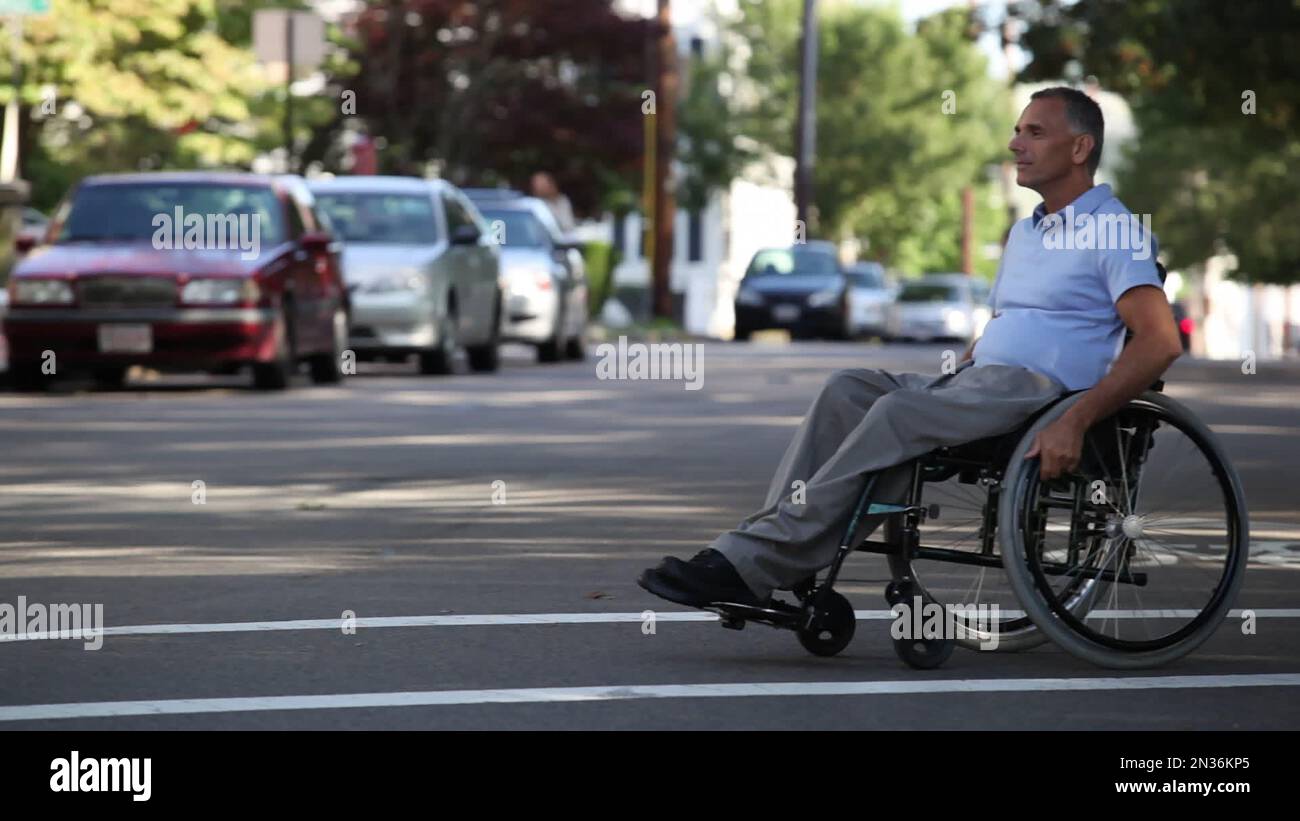 Uomo con lesione al midollo spinale in una strada di attraversamento in sedia a rotelle ad accesso accessibile; Massachusetts, Stati Uniti d'America Foto Stock