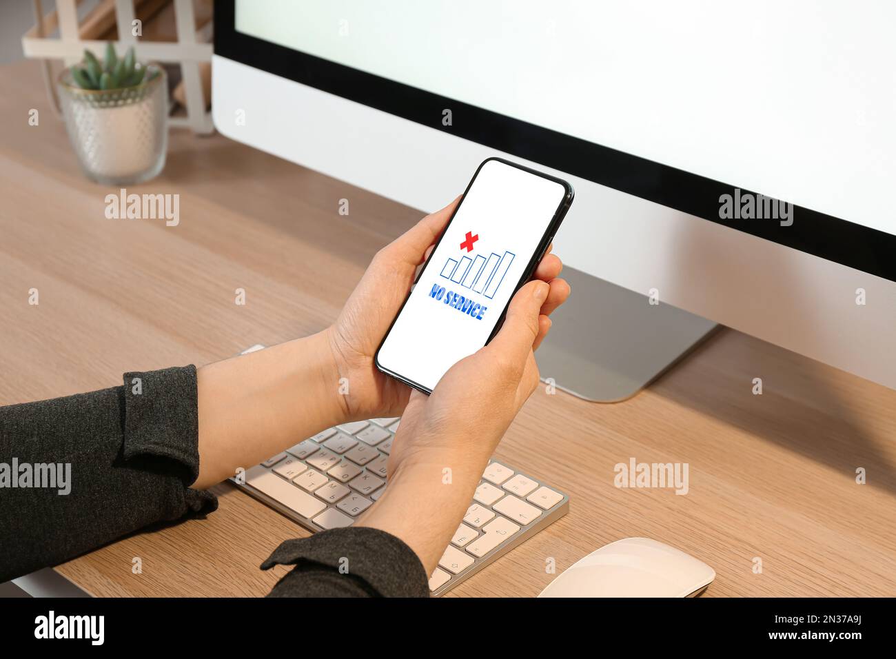 Donna che tiene in mano un telefono cellulare con testo SENZA SERVIZIO sullo schermo sul posto di lavoro Foto Stock