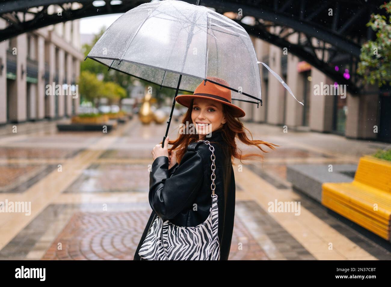 Vista da spalla a positiva donna elegante in cappello di moda camminando  sulla strada della città con ombrello godendo il tempo piovoso all'aperto,  guardando la macchina fotografica Foto stock - Alamy
