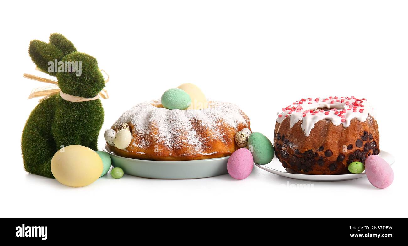Piatti con gustose torte pasquali, uova e coniglietto giocattolo su sfondo bianco Foto Stock