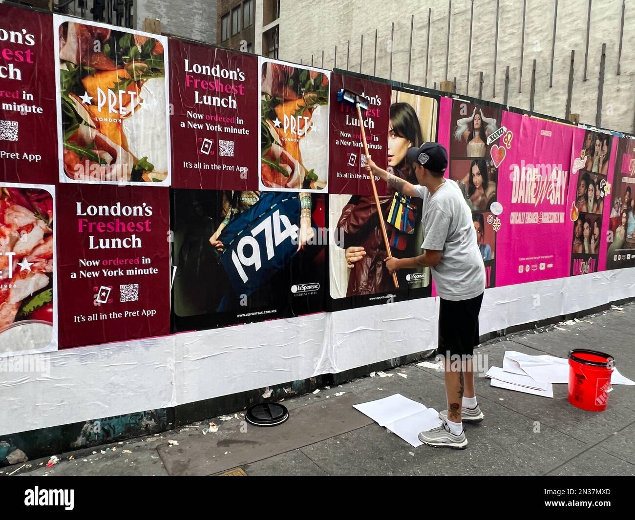 L'operaio mette in su i manifesti di pubblicità su una parete temporanea del luogo di costruzione lungo 6th Avenue nel centro di Manhattan. Foto Stock