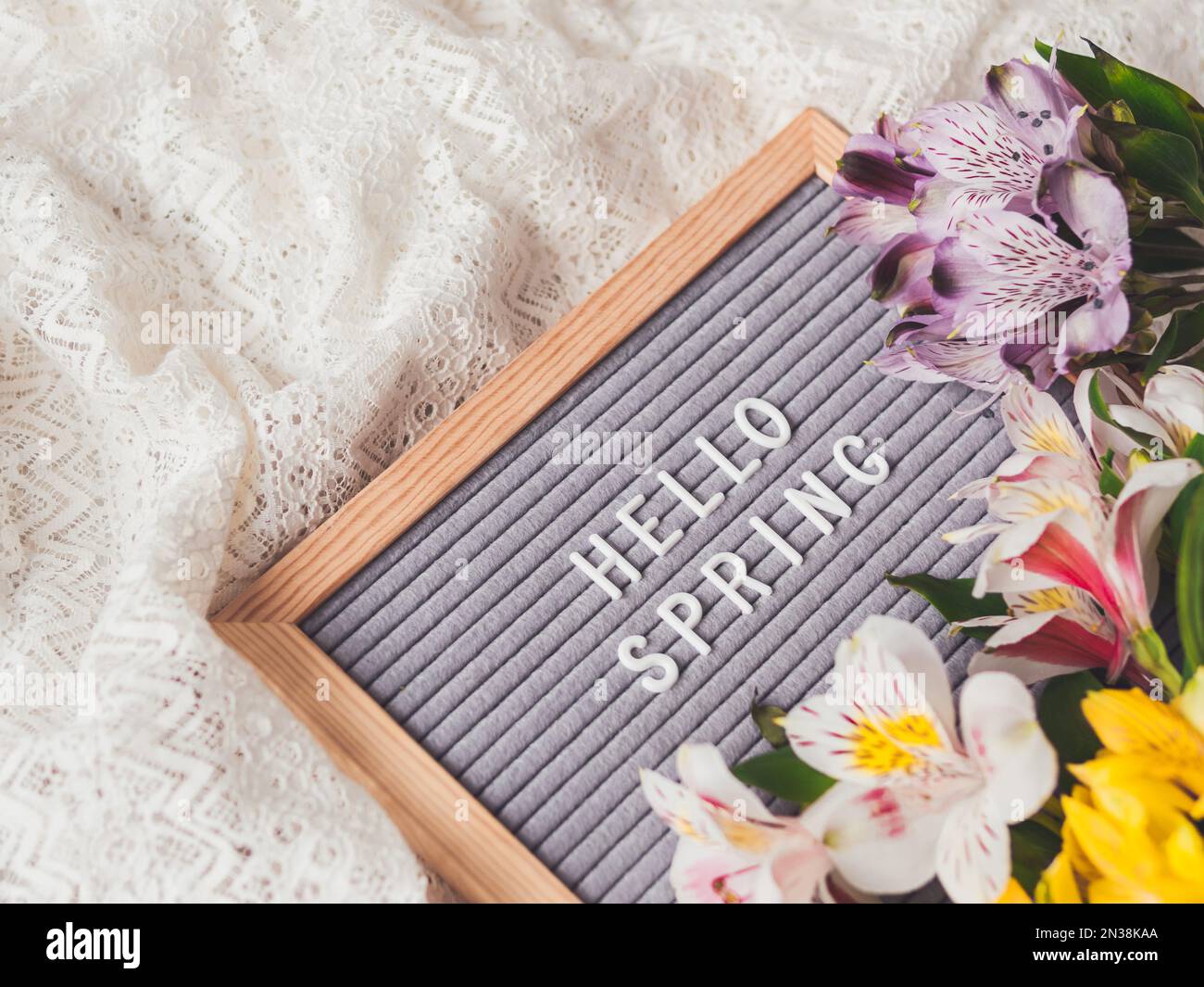 Cartolina con saluto di stagione CIAO PRIMAVERA su pizzi sfondo tessile bianco con fiori freschi di alstroemeria. Foto Stock