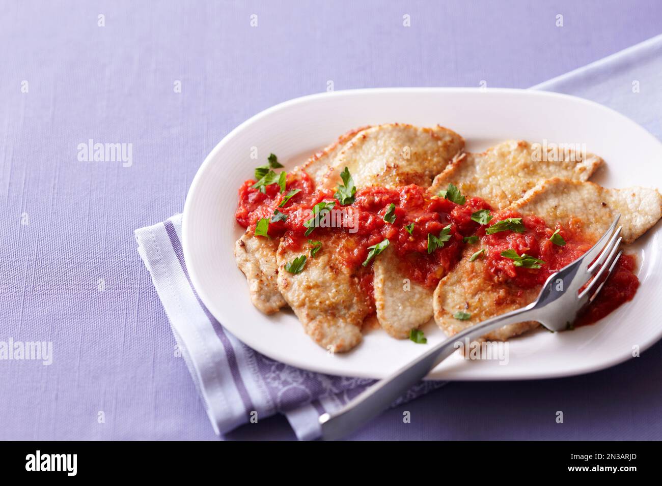 Vitello con salsa di pomodoro su un piatto bianco su sfondo viola Foto Stock