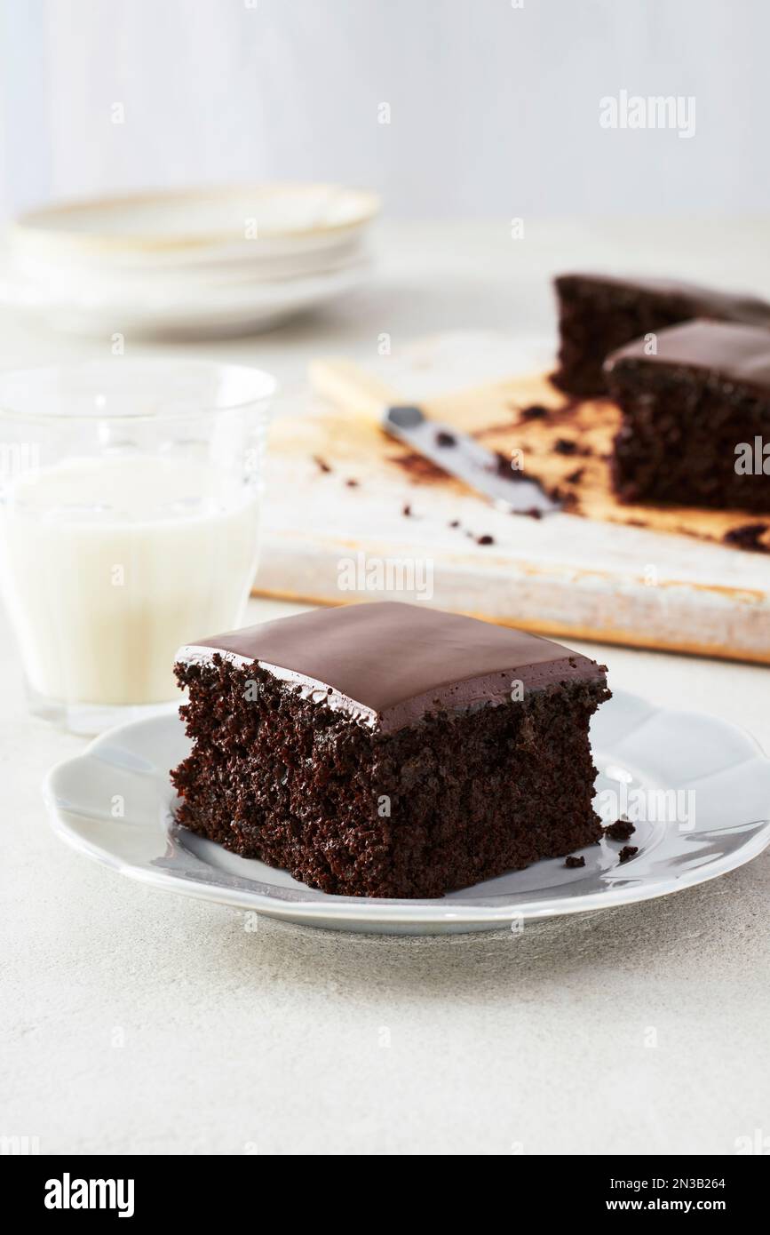 Pezzo di torta al cioccolato fondente con glassa di cioccolato su un piatto da dessert con un bicchiere di latte Foto Stock