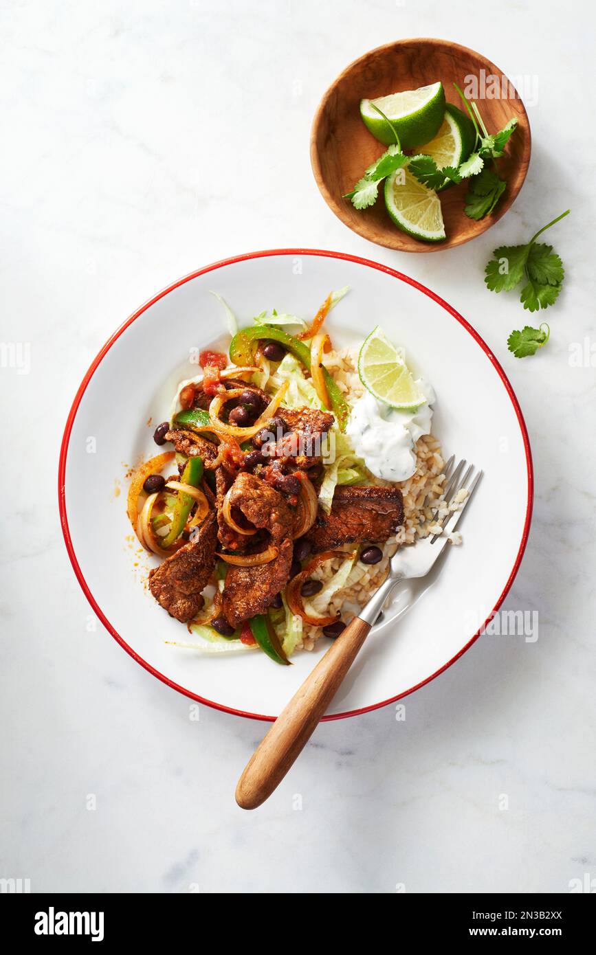 Cena a base di fajita bistecca su un piatto con spicchi di lime e panna acida Foto Stock