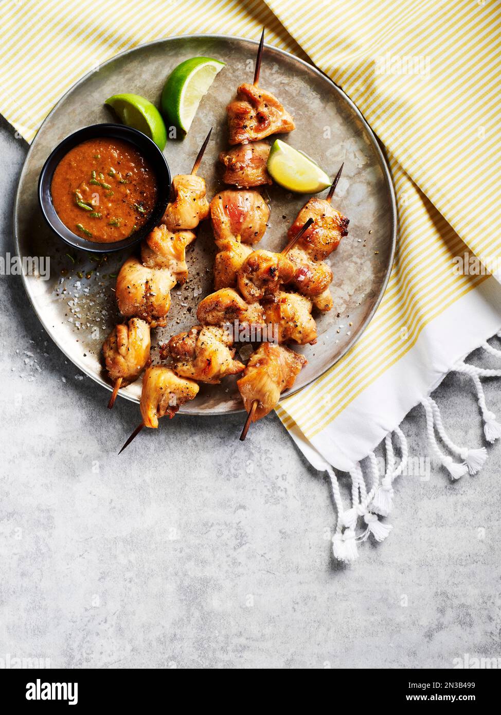 Spiedini di satay di pollo con salsa e spicchi di lime su un vassoio di metallo su tessuto a righe Foto Stock