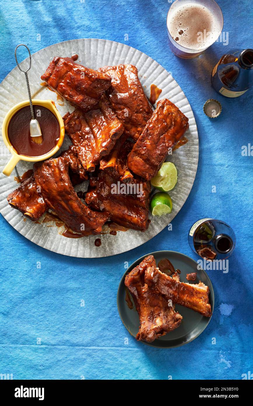 Costolette cotte lentamente con salsa alla griglia e bottiglie di birra su sfondo blu Foto Stock