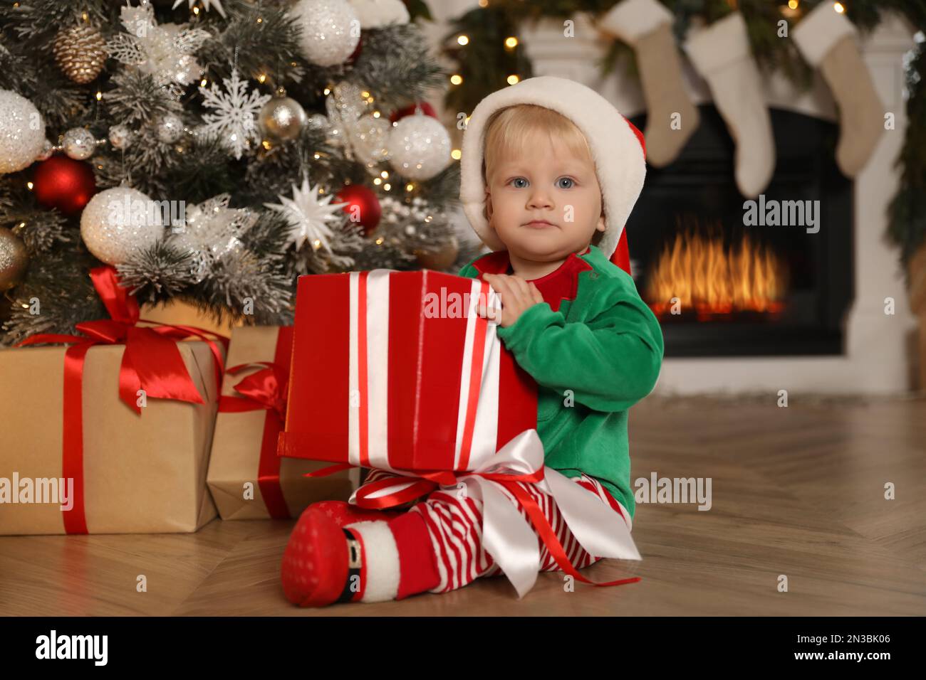 Cute bambino in vestiti di elfo del Babbo Natale che tiene la scatola del  regalo vicino all'albero di Natale nel paese Foto stock - Alamy