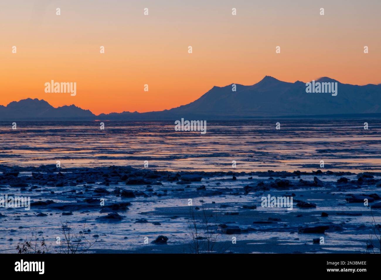 Tramonto invernale visto dal centro di Anchorage, guardando attraverso l'insenatura del monte Spurr e i Monti Tordrillo in silhouette, con pezzi di ghiaccio e... Foto Stock