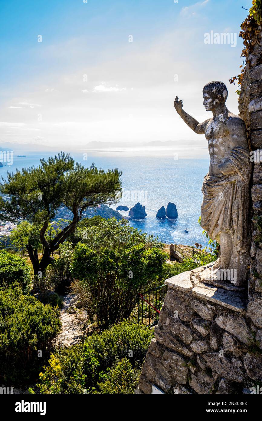 Statua dell'imperatore romano Tiberio con vista sulla baia dei Faraglioni e sulle formazioni rocciose dal Monte Solaro sull'isola di Capri; Napoli, Capri, Italia Foto Stock