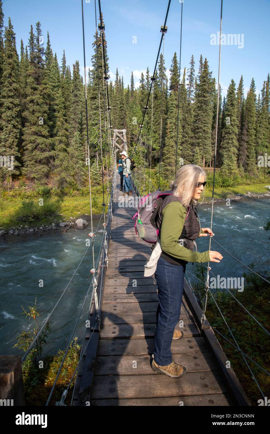 Escursionisti che attraversano il ponte sospeso di Riley Creek sul Triple Lakes Trail Foto Stock