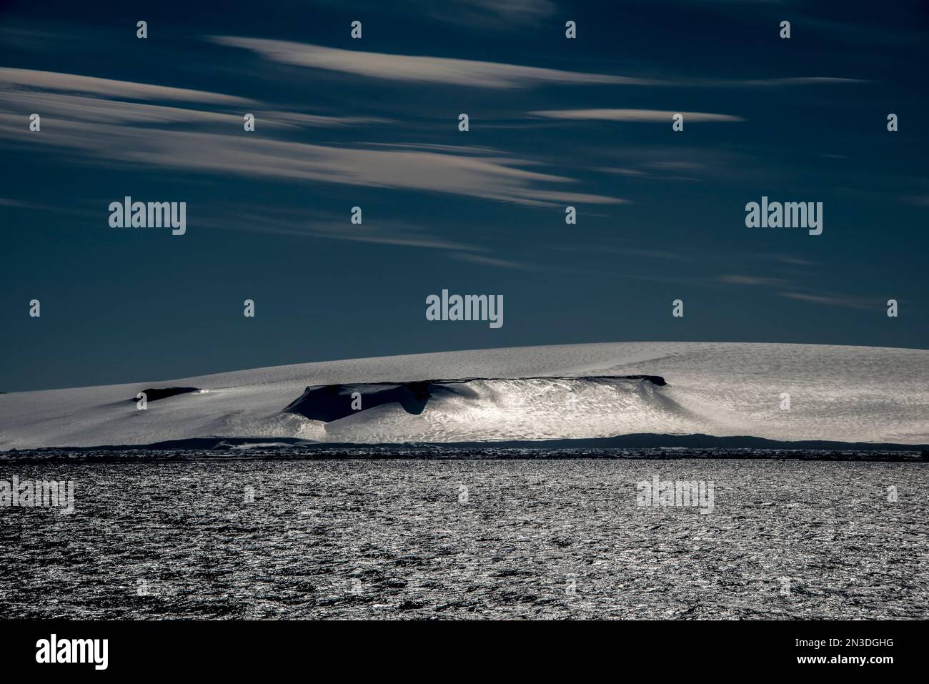 Il sole si riflette sul ghiaccio e sulla neve su un'isola di Anderson bagnata dal vento nello stretto antartico; Antartide Foto Stock