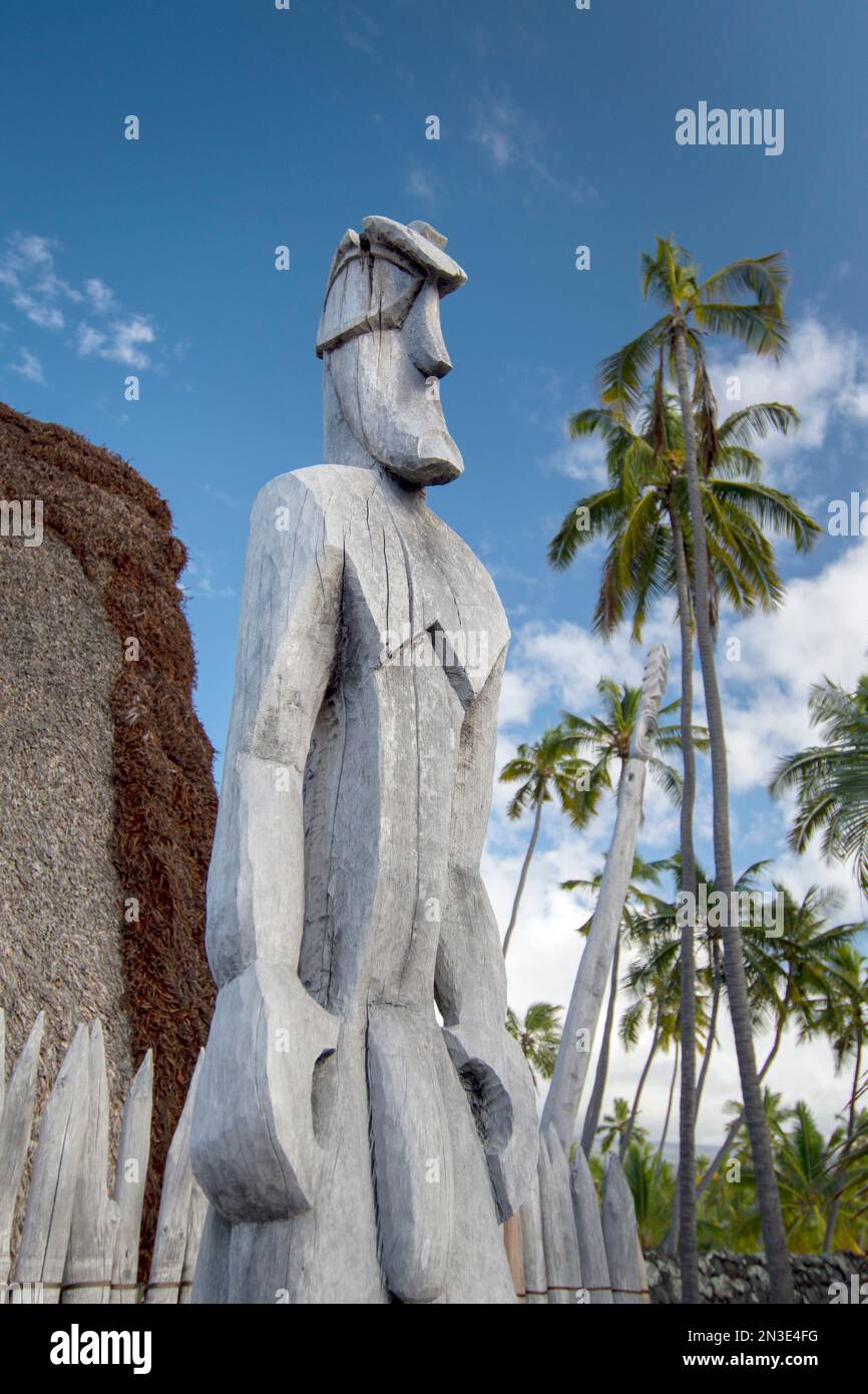 Statua in legno (ki'i) di una divinità hawaiana di fronte a un edificio con tetto di paglia nel Parco Nazionale PU'uhonua o Hōnaunau, una delle anci meglio conservate... Foto Stock