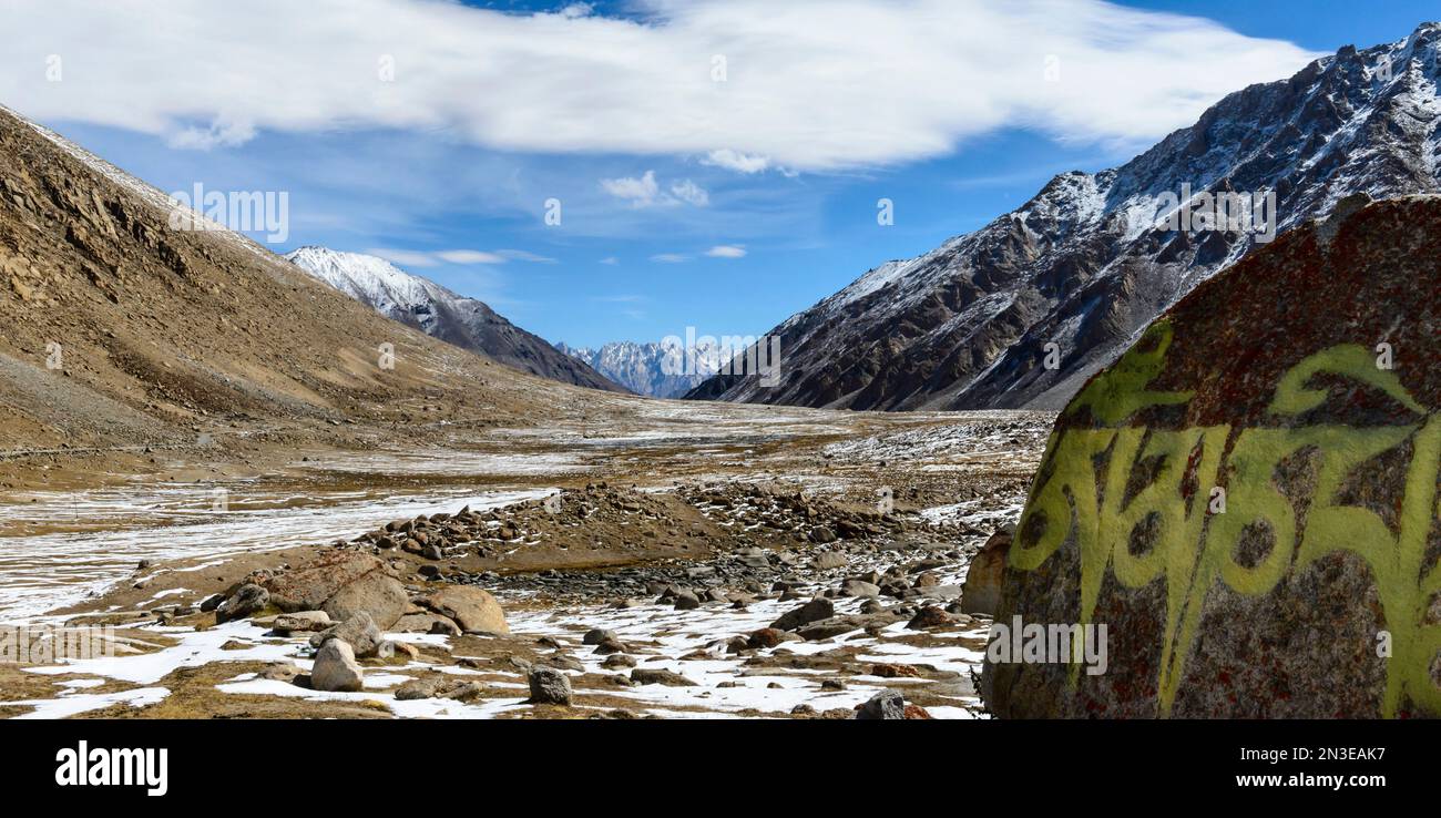 Valle ghiacciata con mantra dipinto su roccia e montagne innevate alle pendici dell'Himalaya nella regione di Ladakh Foto Stock