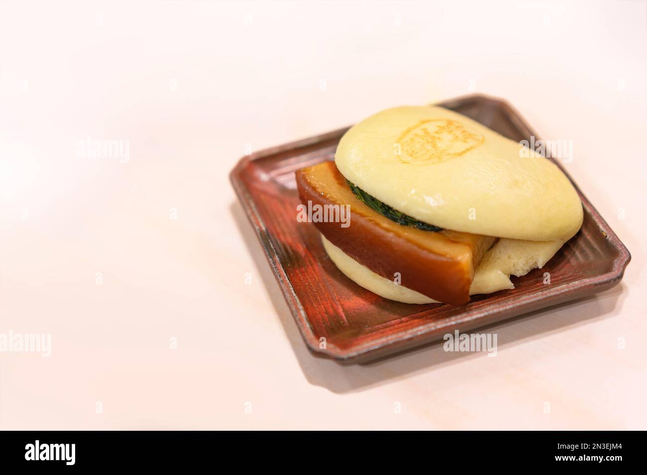 Un giapponese cotto a vapore Bun Kakuni Manju su un piatto su un tavolo riempito con tenera, lentamente brasato pancia di maiale, fornendo un delizioso boccone, ancora una via amata Foto Stock