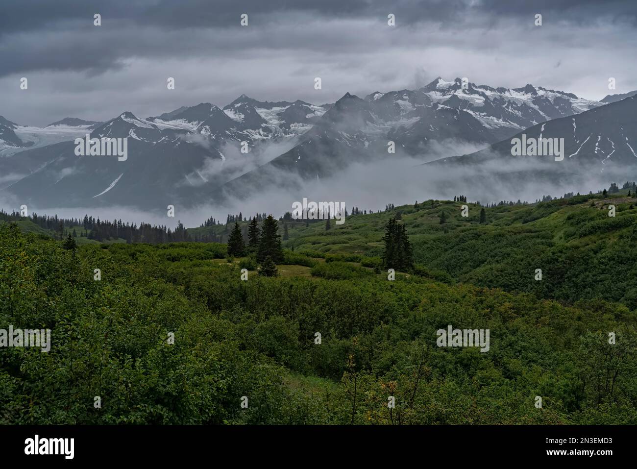 Basse nuvole appese alla base del crinale montano con arbusti verdi nelle pianure, creano un ambiente tranquillo al passo Haines lungo il ... Foto Stock