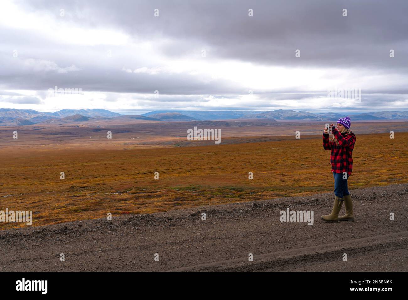Donna che scatta foto con il cellulare lungo la Dempster Highway e si gode il paesaggio nello Yukon canadese; Dawson City, Yukon, Canada Foto Stock