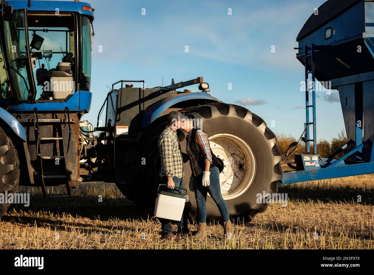 Una moglie porta il marito a pranzo al taxi di un trattore e gli dà un bacio mentre sono impegnati con la raccolta di canola autunnale Foto Stock