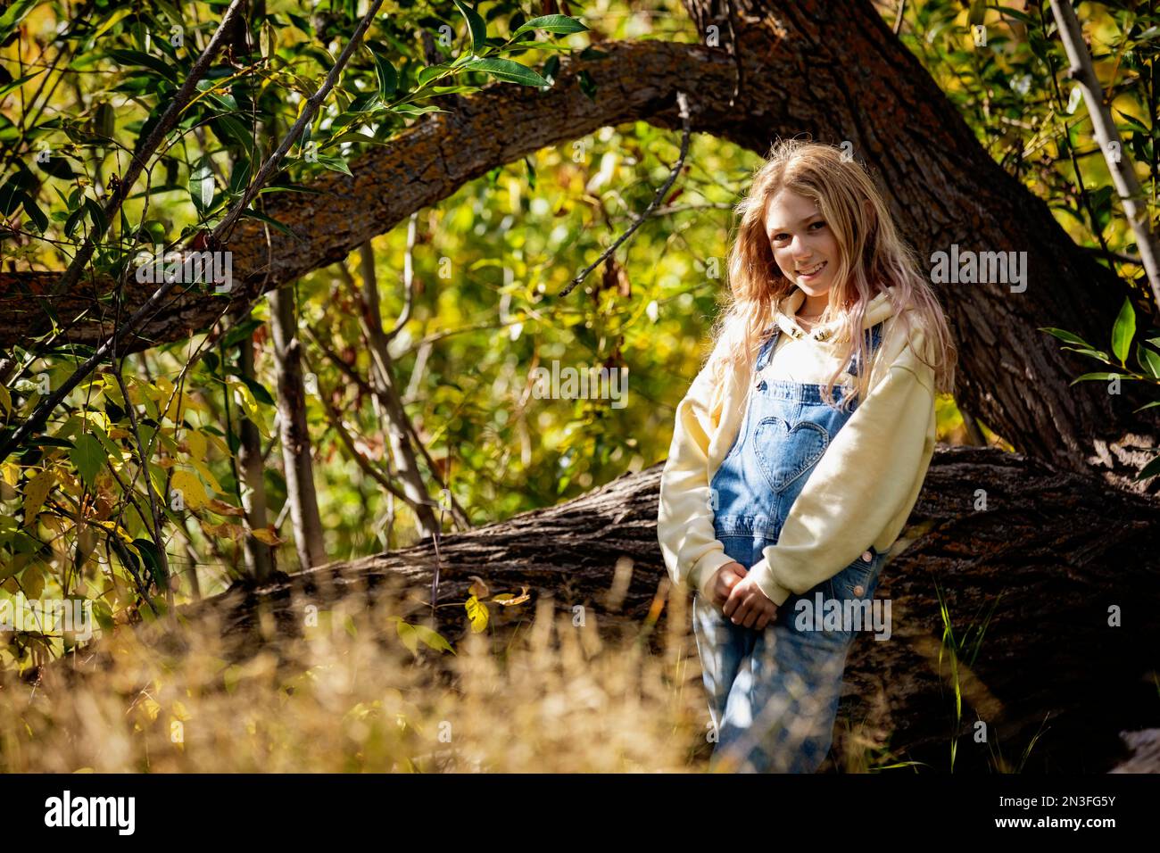 Giovane ragazza che posa per una foto in una foresta durante una gita in famiglia in una calda giornata autunnale in un parco cittadino; St Albert, Alberta, Canada Foto Stock