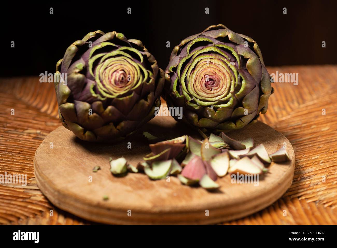 Carciofi viola su sfondo di legno. Carciofi con la parte superiore tagliata. Preparazione per la cottura. Cibo vegano sano. Foto Stock