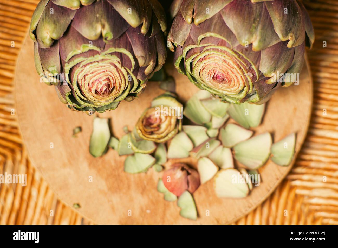 Carciofi viola su sfondo di legno. Carciofi con la parte superiore tagliata. Preparazione per la cottura. Cibo vegano sano. Foto Stock