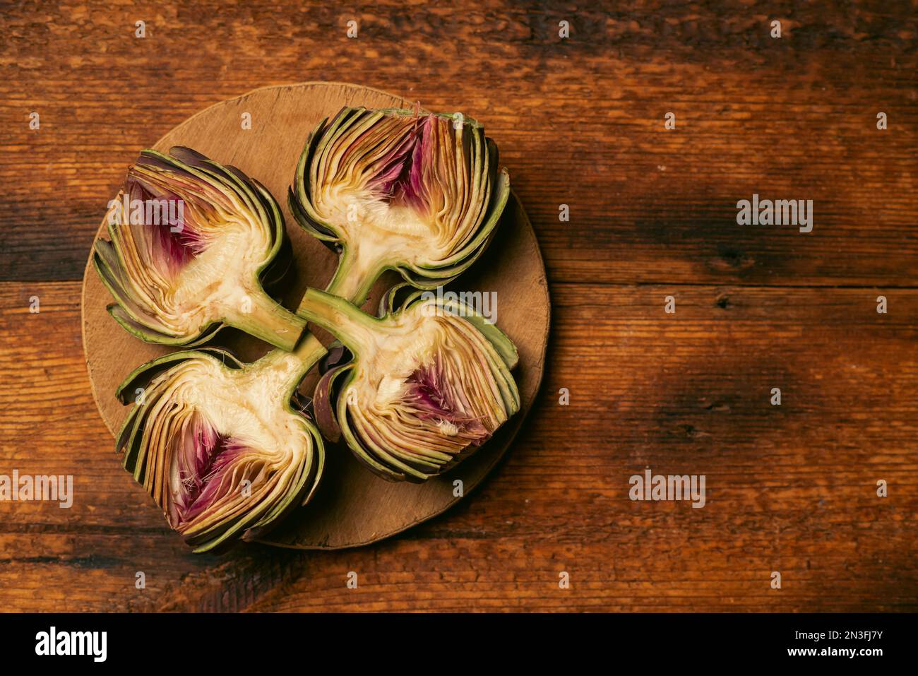 Carciofi viola su sfondo di legno. Carciofi con la parte superiore tagliata. Preparazione per la cottura. Cibo vegano sano. Foto Stock