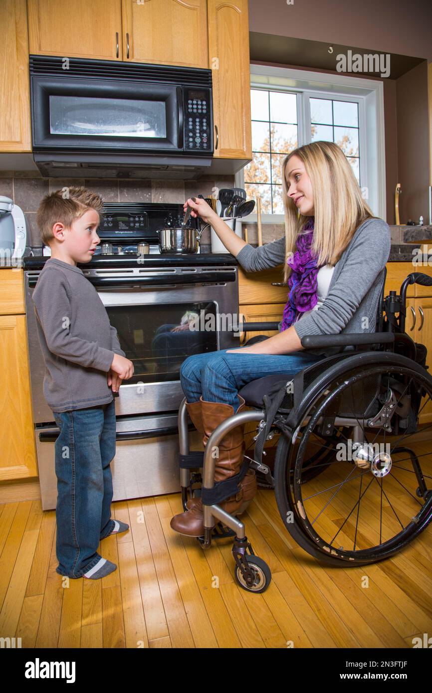 Giovane donna disabile che parla con il suo giovane figlio mentre cucina in cucina a casa; Spruce Grove, Alberta, Canada Foto Stock