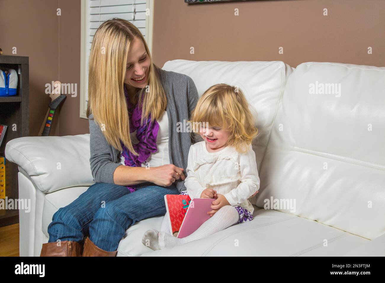 La giovane madre disabile si siede sul divano a casa a leggere con la sua figlia, Spruce Grove, Alberta, Canada Foto Stock