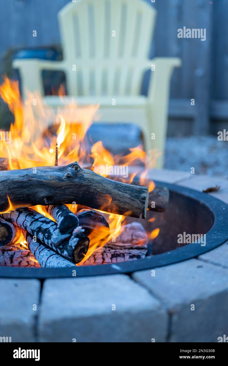 Ripresa verticale di una fossa di fuoco in pietra in una giornata autunnale con una sedia da giardino gialla sullo sfondo sfocato Foto Stock