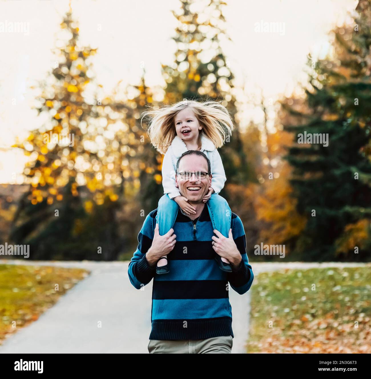 Un padre che porta la figlia sulle spalle mentre cammina in un parco cittadino durante la stagione autunnale; St Albert, Alberta, Canada Foto Stock