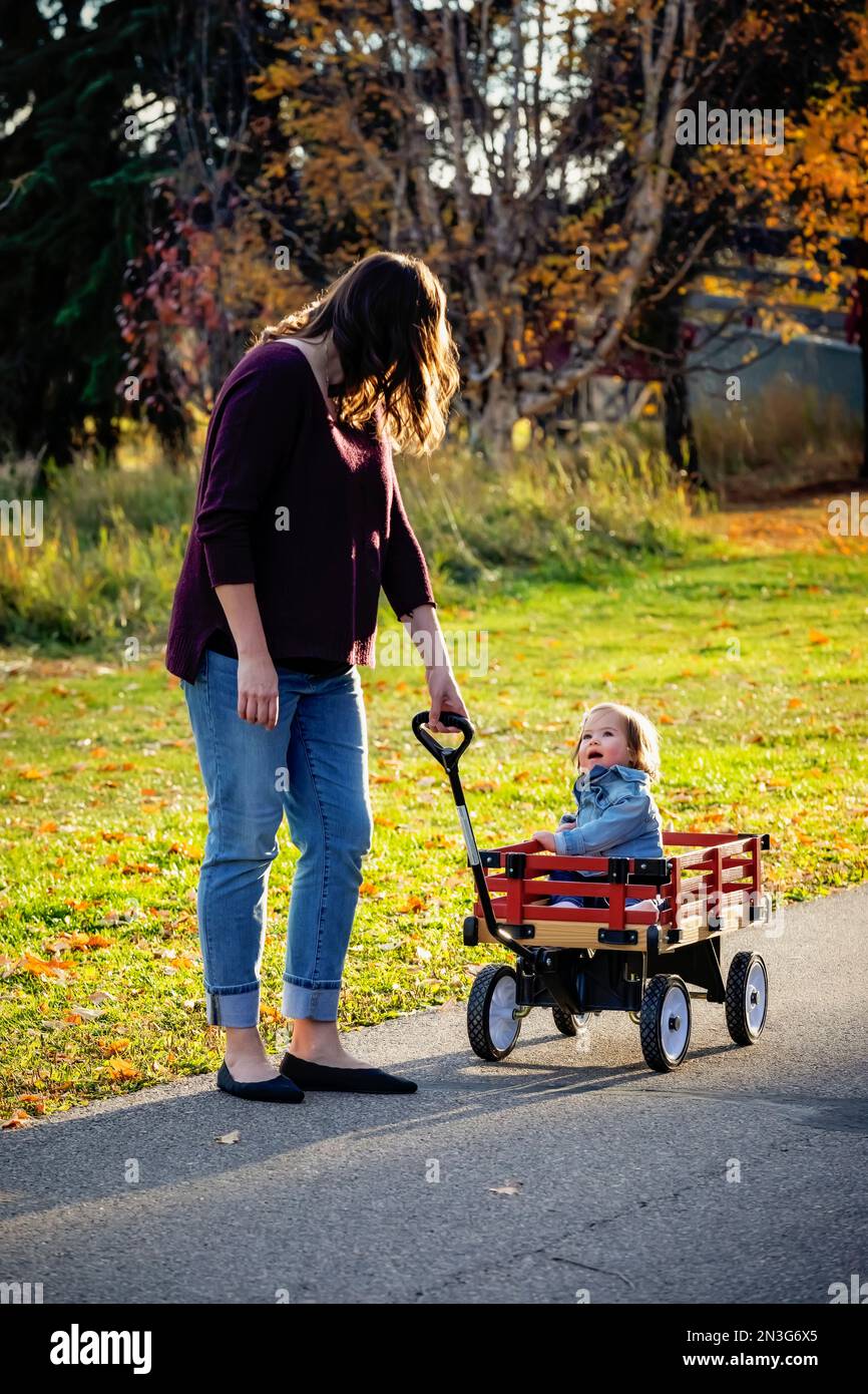 Una madre che tira il suo bambino con la sindrome di Down in un carro in un parco cittadino durante la stagione autunnale; St, Albert, Alberta, Canada Foto Stock