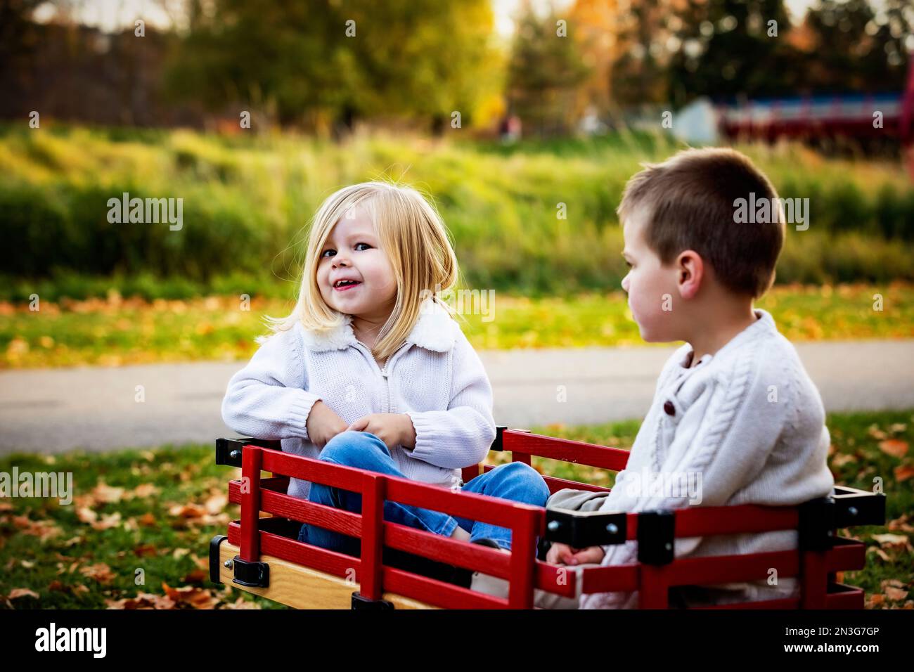 Giovane ragazza e suo fratello in un carro in un parco cittadino lungo un fiume durante la stagione autunnale; St Albert, Alberta, Canada Foto Stock