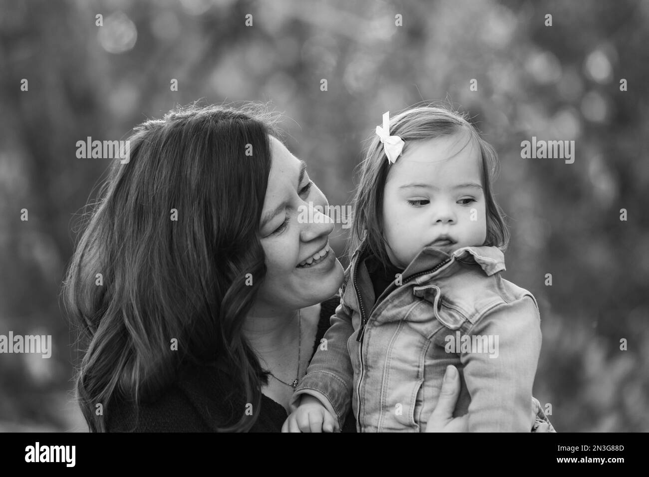 Ritratto di una madre e della sua bambina con la sindrome di Down che trascorrono del tempo all'aperto durante una gita in famiglia in un parco cittadino Foto Stock