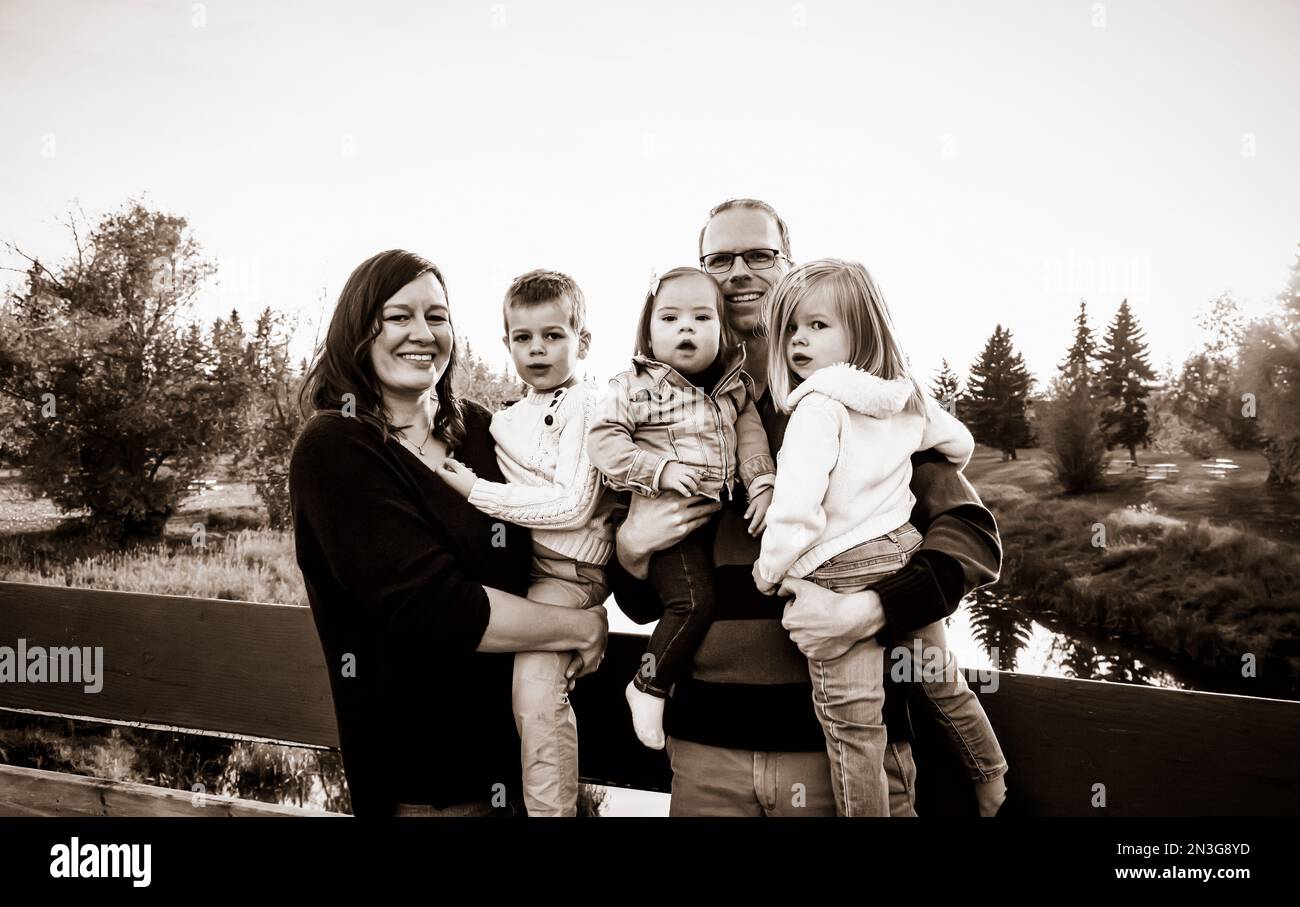 Ritratto di una giovane famiglia con tre figli, figlia bambina con la sindrome di Down, in un parco cittadino durante la stagione autunnale; St Albert, Alberta, Canada Foto Stock