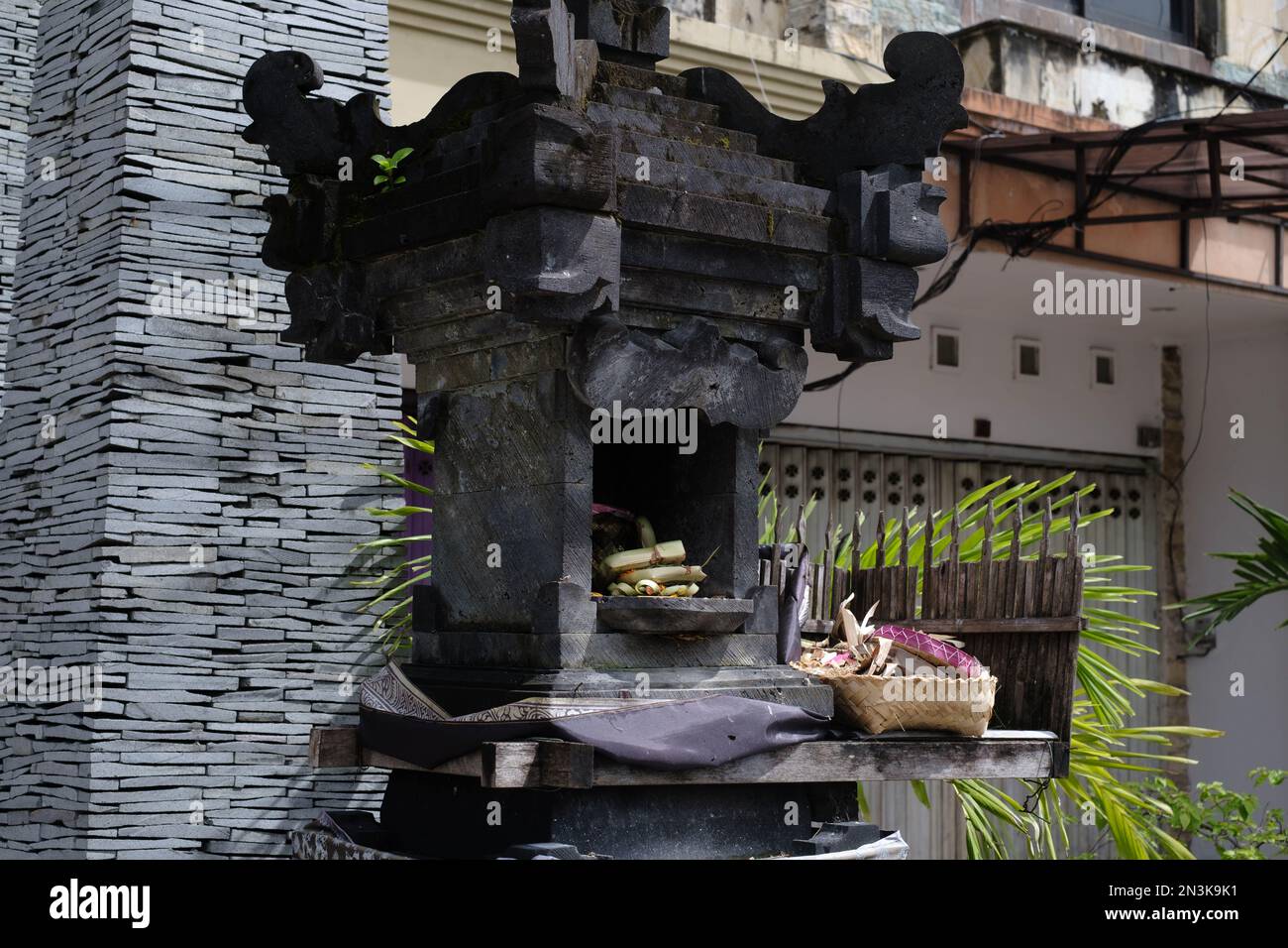 Un canang sari splendidamente organizzato che offre riposi in una tradizionale casa di spirito Balinese, circondato da incenso e fiori Foto Stock